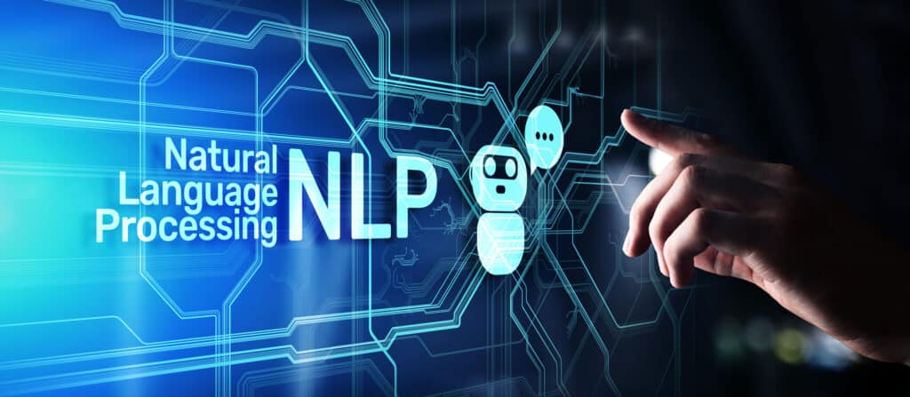 Close-up of a human’s hand reaching to press a chatbot icon on a blue, digital sign reading, “Natural Language Processing” and “NLP”.