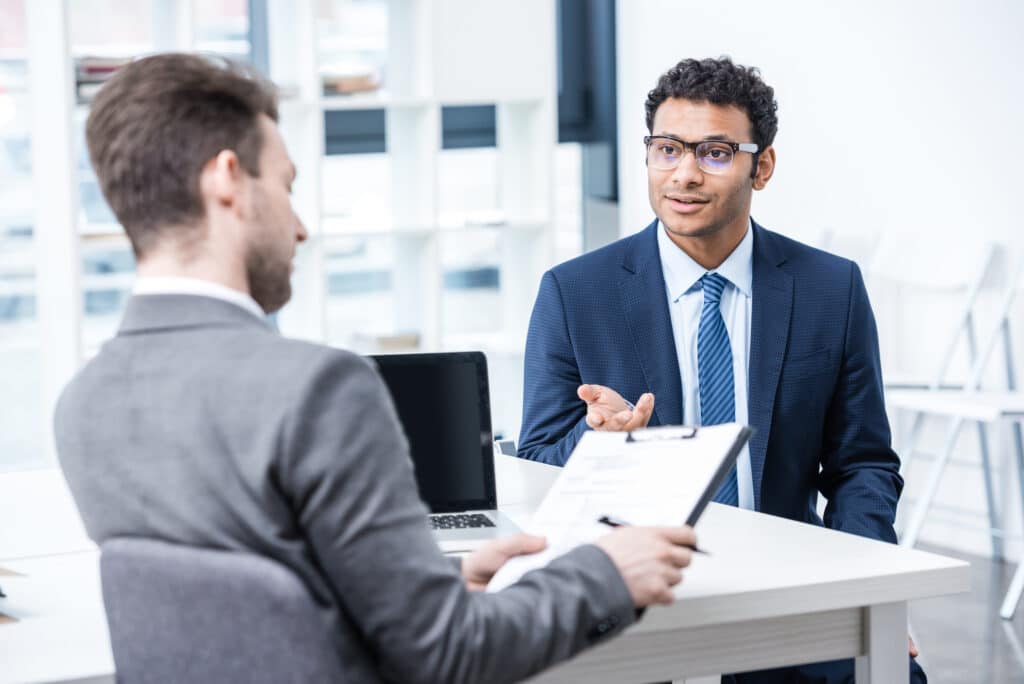 An interviewer looks at their clipboard as a well-dressed job candidate answers a question.