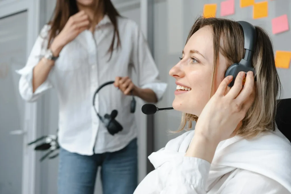 A contact center agent smiles while on her headset, while another contact center agent gestures in the background