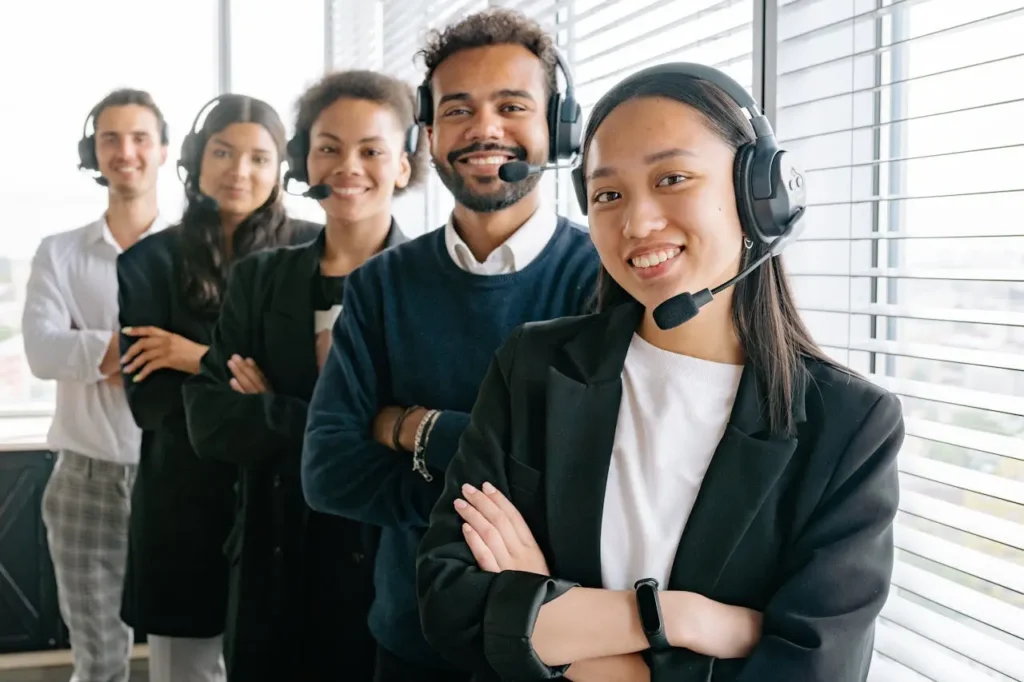 A row of five contact center agents stand with their arms crossed and smile at the camera, satisfied with their call center AI solutions